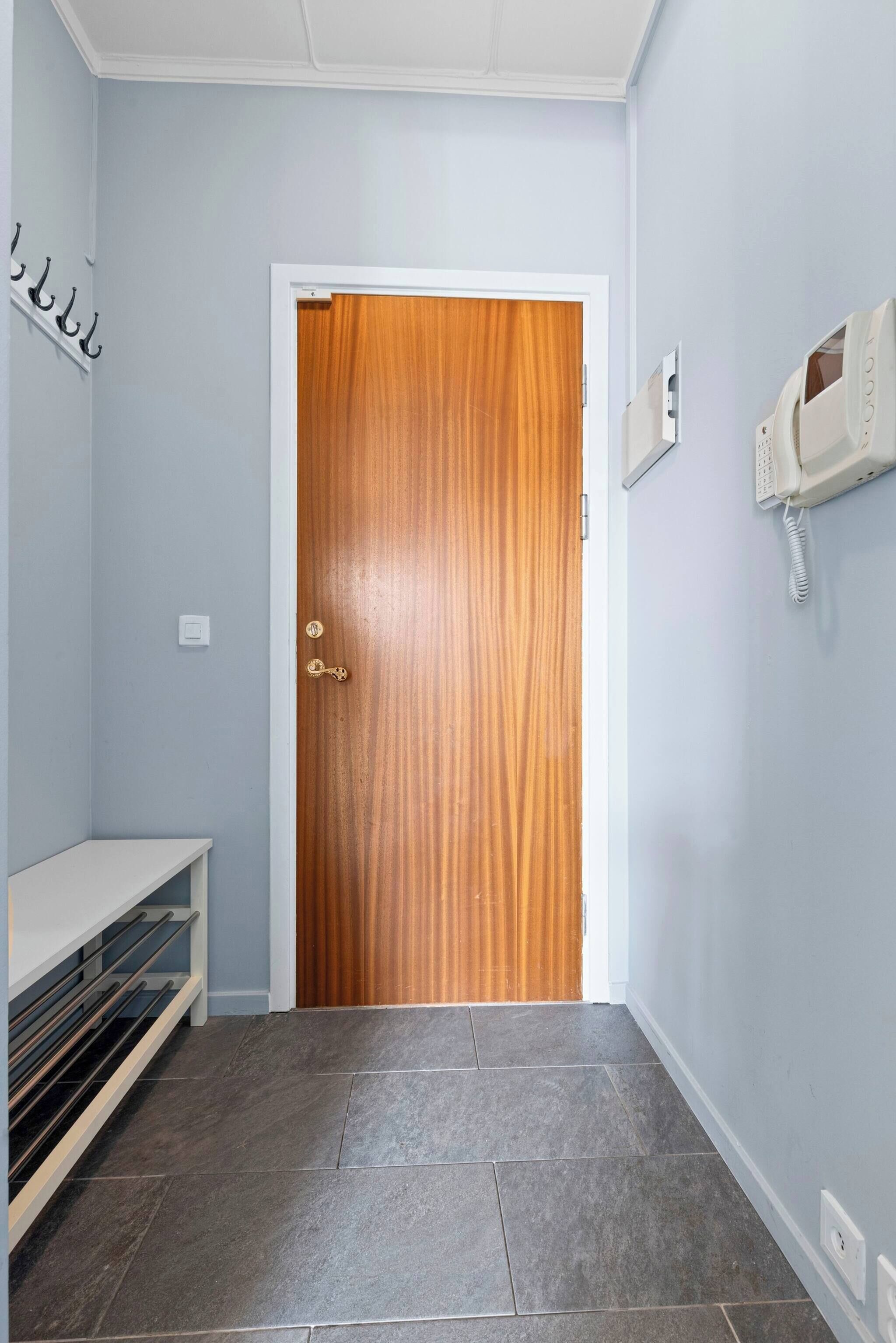 Ein Flur mit Holztür, weißer Bank, Telefon und Lichtschalter an der Wand.