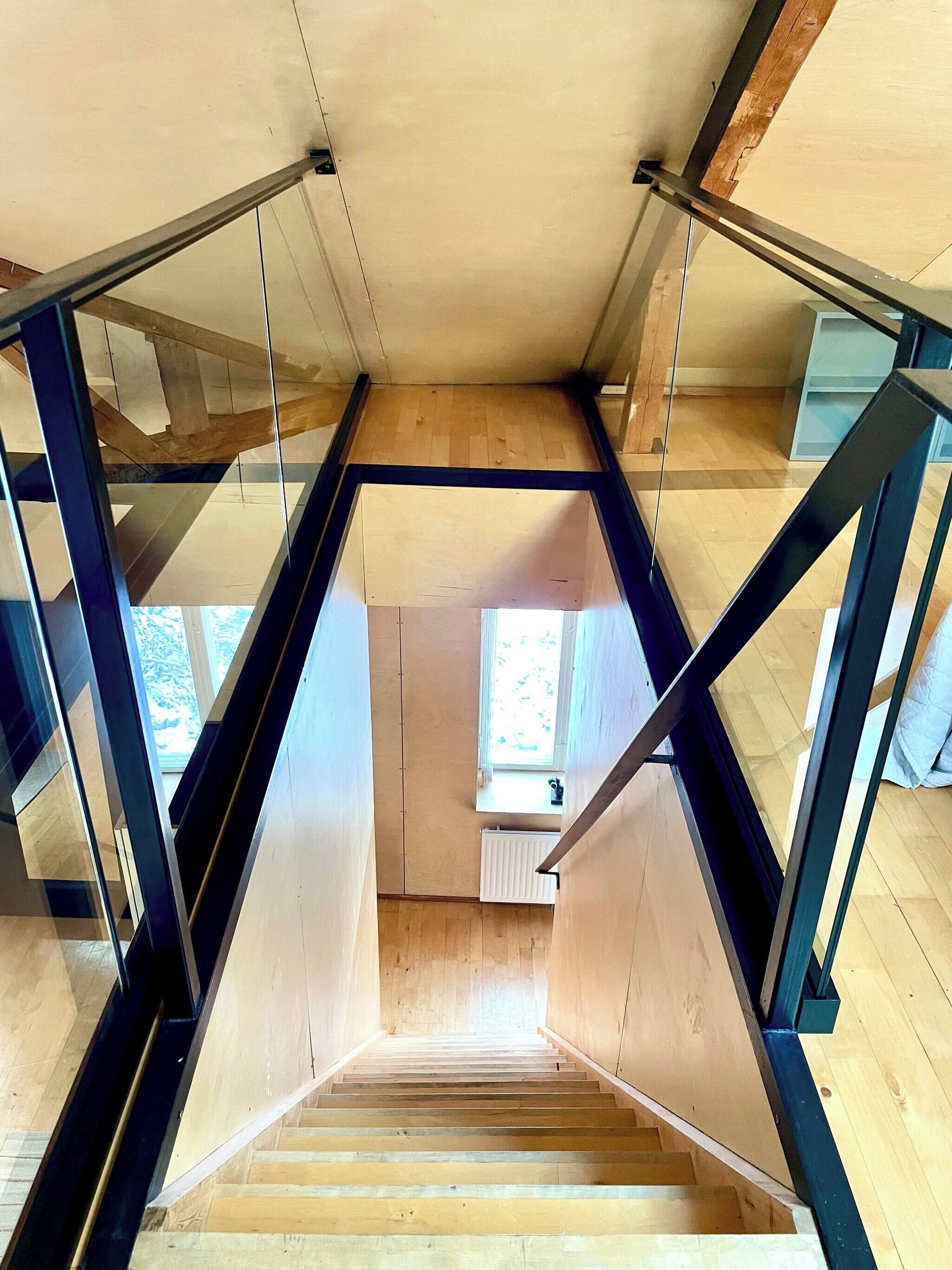 A wooden staircase with glass railings leading to a high ceiling.