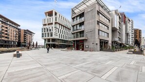 Ein moderner Stadtplatz mit einem großzügigen, offenen Bereich, umgeben von mehrstöckigen Gebäuden mit Geschäftsräumen.