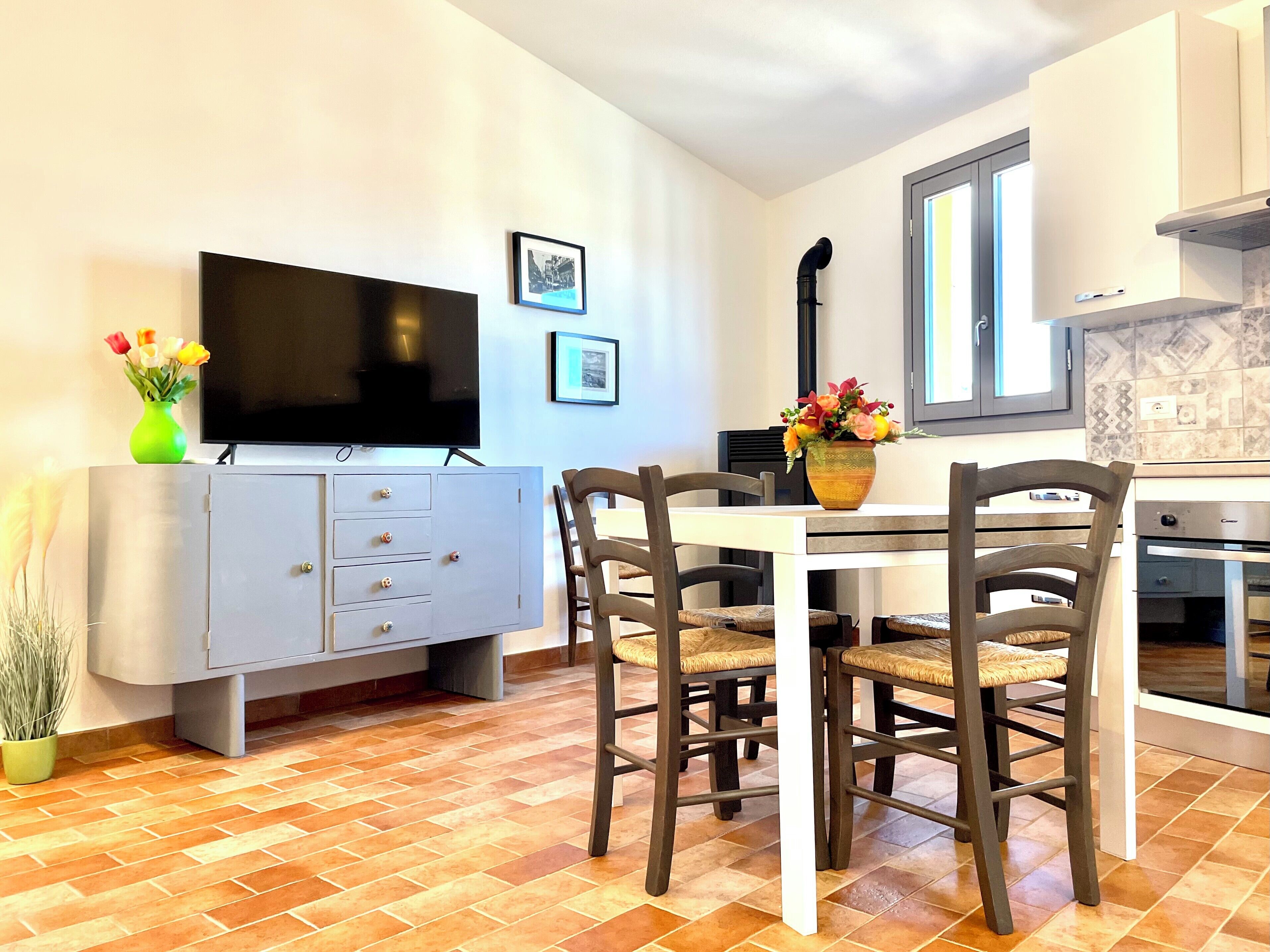A compact living space with a dining table, chairs, a TV, a cabinet, and a kitchen area.