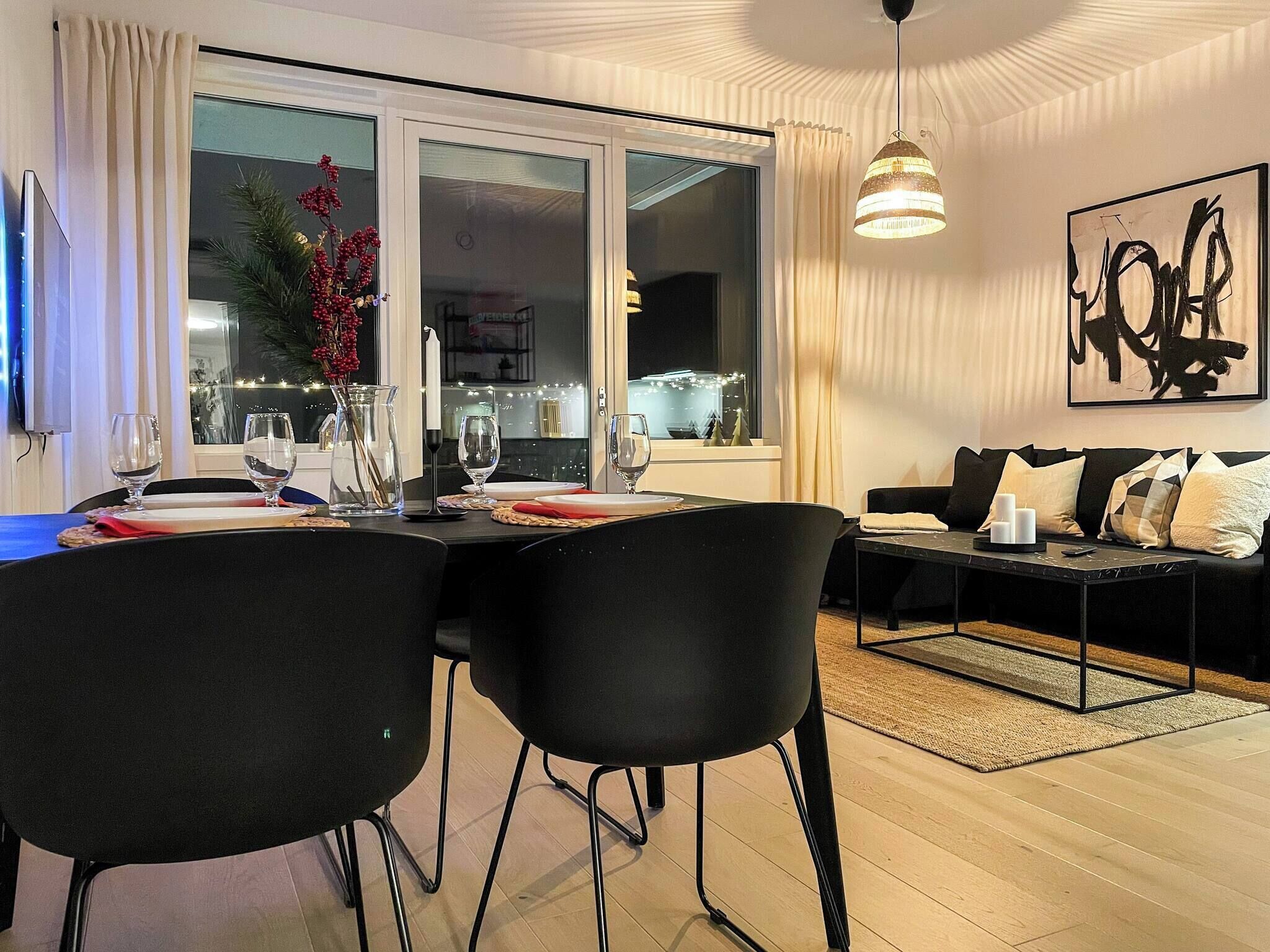 A modern dining area with a table set for two, a sofa, and a large window with curtains.