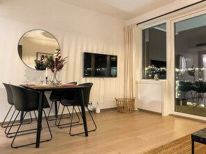 A modern dining area with a round mirror, a dining table set with chairs, and a view of the city at night through large windows.
