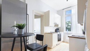 Una cocina moderna con armarios blancos, una pequeña zona de comedor con mesa y sillas, y un ventanal que proporciona luz natural.