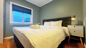 A neatly made bed with white linens and rolled towels, a bedside lamp, and a nightstand with drawers. - Cozy 2BR Apartment With Parking (Oslo)