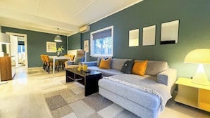 A modern living room with a grey sofa, a coffee table, and a dining area with chairs and a table. - Cozy 2BR Apartment With Parking (Oslo)