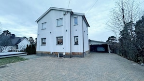 A two-story building with a garage entrance, a brick driveway, and a small front yard. - Cozy 2BR Apartment With Parking (Oslo)