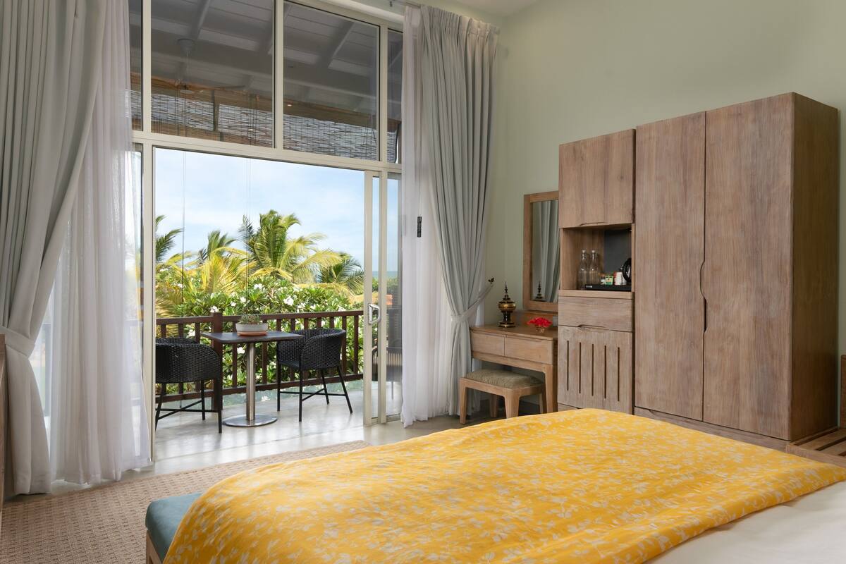 Une chambre comprenant un lit, une armoire en bois, un bureau avec un miroir et un balcon avec une table et des chaises.