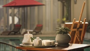 A table with a tea set and a potted plant, a red umbrella, and lounge chairs by a pool. - Ayuda Sanctuary Boutique Negombo (Negombo)