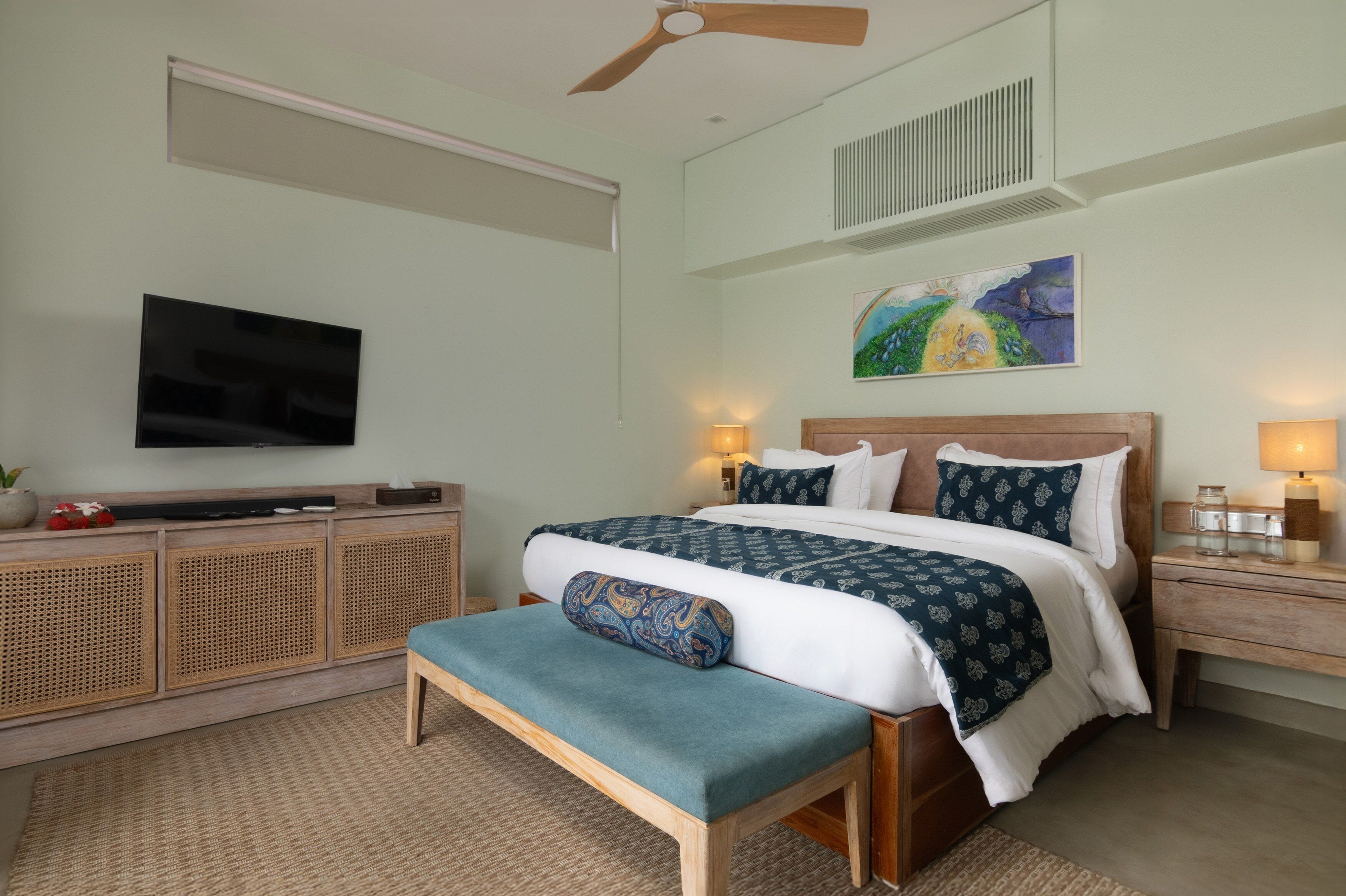 A bedroom with a bed, bedside tables, a TV, a ceiling fan, and a painting on the wall.