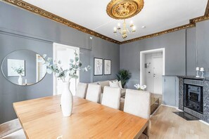 A dining room with a wooden table, white chairs, a vase with flowers, and a fireplace with a stone mantle. - Big and Bright Apartment in the Center (Oslo)