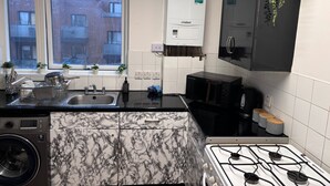A modern kitchen with a gas stove, a microwave, a sink, and a window with a view of a brick building. - 1br-sleeps4-35mintocentrallondon-40mintoheathrow (London)