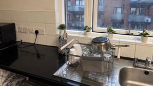 A kitchen with a black countertop, a sink, a window with potted plants, and a view of a brick building. - 1br-sleeps4-35mintocentrallondon-40mintoheathrow (London)