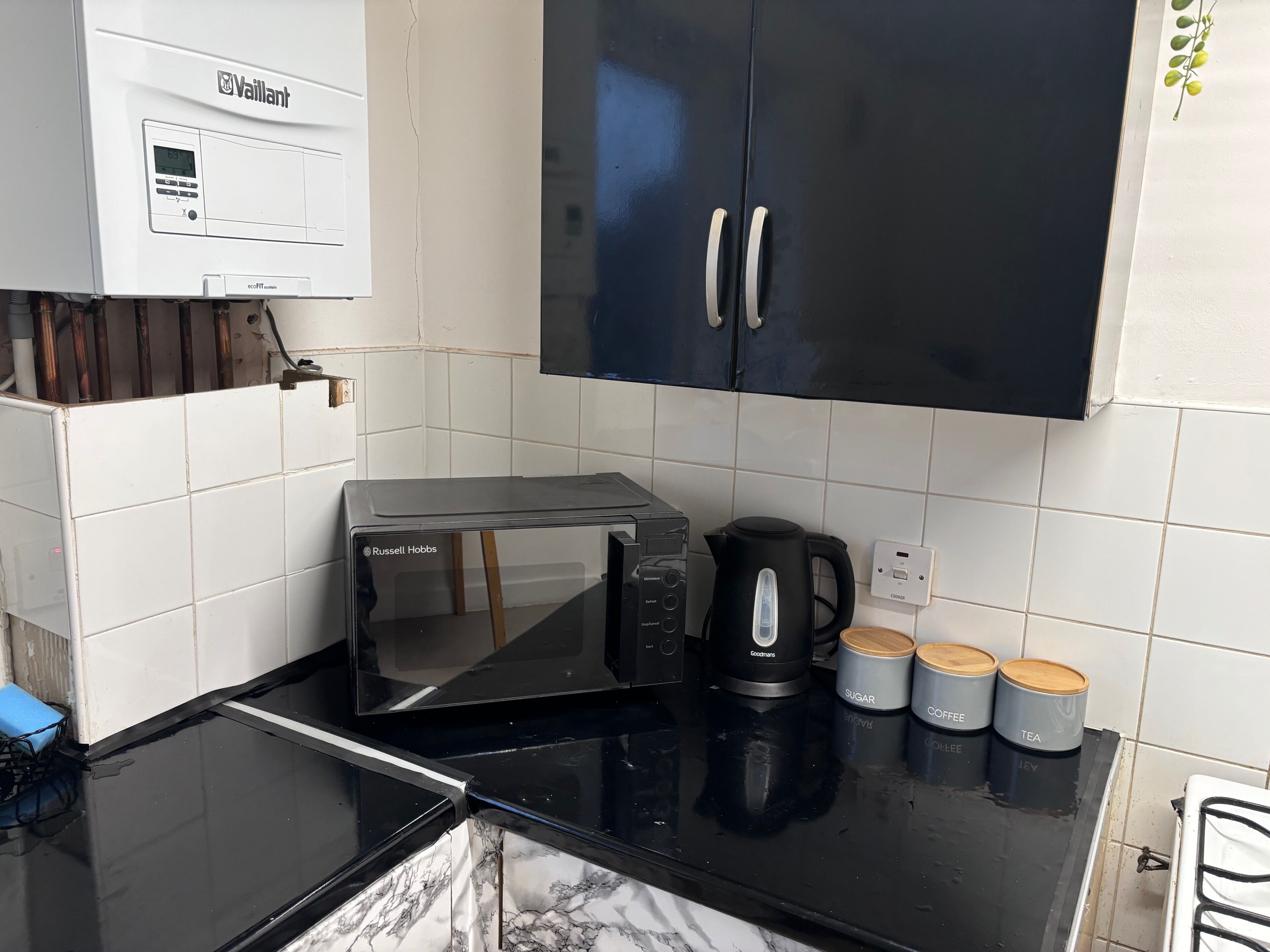 A kitchenette with a black countertop, a toaster, a kettle, and three containers labeled sugar, coffee, and tea.