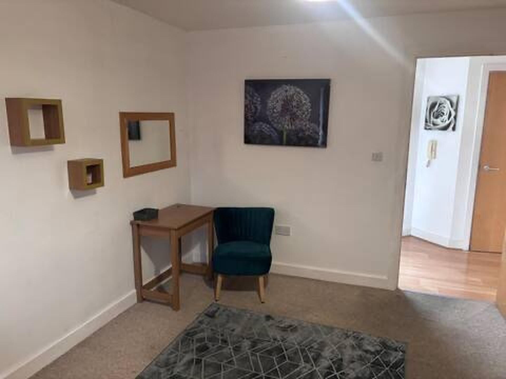 Une pièce avec un bureau en bois, une chaise bleue, un tapis à motifs géométriques et un tableau encadré accroché au mur.