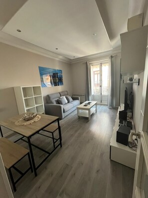 A modern living room with a grey sofa, a coffee table, a TV stand, and a painting on the wall. - Apartment between Malasaña and Plaza España (Madrid)
