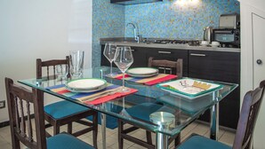 A dining area with a glass table, chairs, and a kitchen in the background. - Camula Inn (Catania)