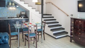 A modern kitchen with a dining area, a staircase, and a TV mounted on the wall. - Camula Inn (Catania)