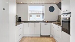 Et moderne køkken med hvide skabe, en Bosch opvaskemaskine, en Siemens ovn og et stort vindue med skodder.