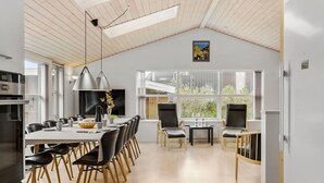 Et moderne køkken med spiseplads, store vinduer og et højt loft med ovenlys.