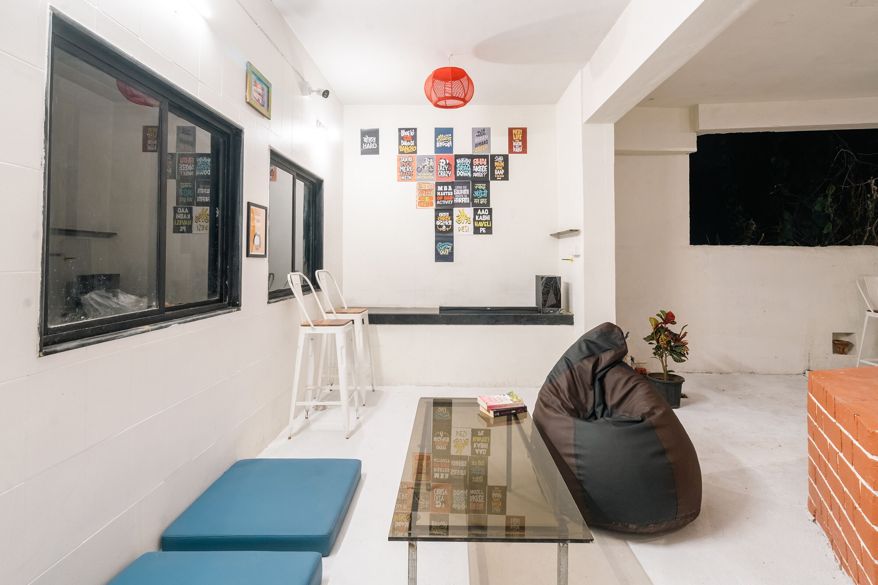 A modern living room with a glass coffee table, a black bean bag, a blue sofa, and a brick wall.