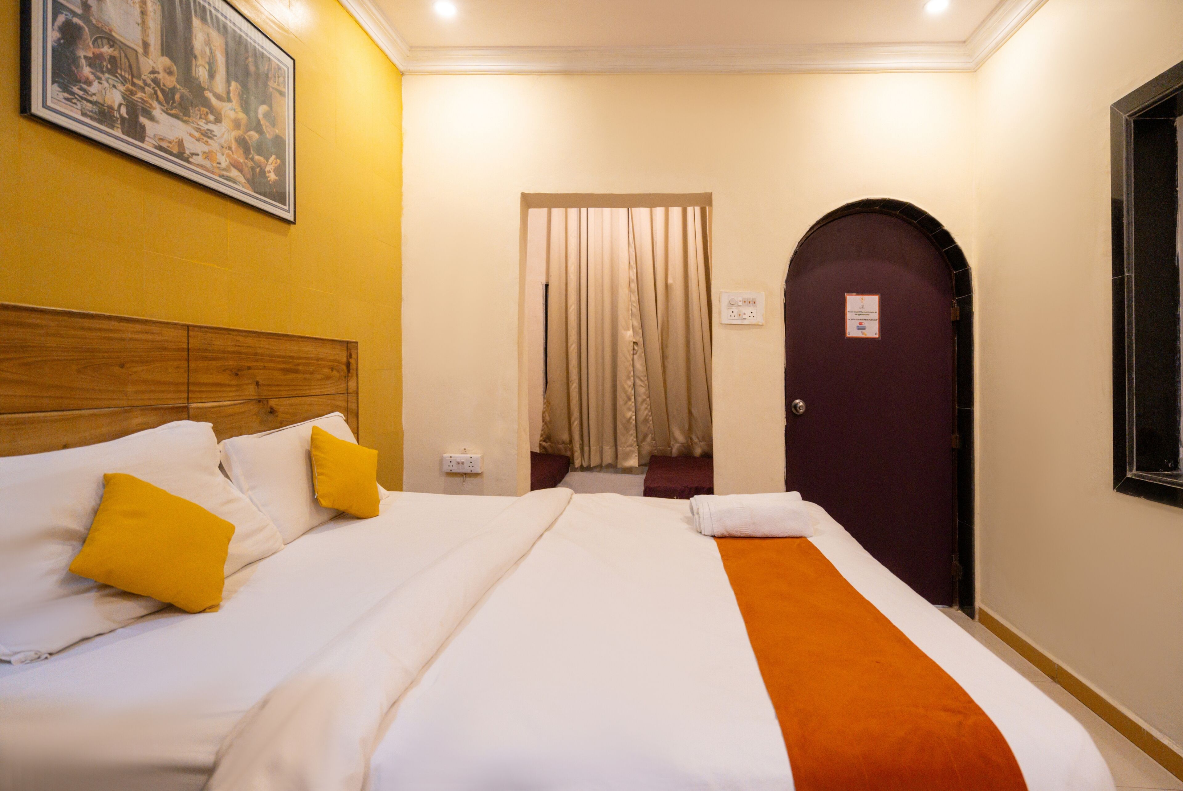 A hotel room with a bed, a wooden headboard, a painting on the wall, a door, and a window.