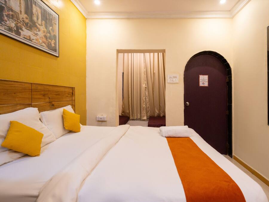 A hotel room with a bed, a wooden headboard, a painting on the wall, a door, and a window.