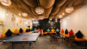 A ping pong table, seating area with cushions, and hanging light fixtures in a room. - Moustache Daman (Daman)