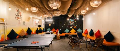 Una mesa de ping pong, una zona de estar con cojines e lámparas colgantes en una habitación.