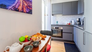 A modern kitchen with grey cabinets, a stainless steel oven, and a dining area with a table set for breakfast.