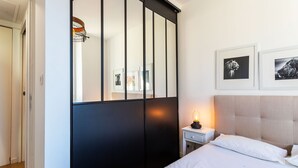 A bedroom with a bed, a nightstand, a lamp, a wardrobe, and two framed pictures on the wall.