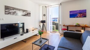 A modern living room with a flat-screen TV, a sofa, a coffee table, and a dining area with a table and chairs.