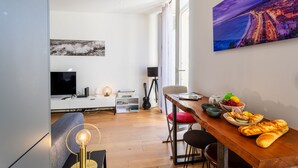 A modern living room with a flat-screen TV, a guitar, and a dining area with a wooden table and chairs.