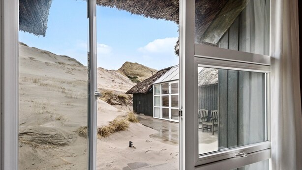 A beach house with a thatched roof, a large glass door, and a view of the beach and dunes. - Lovely home in Hvide Sande with sauna (Hvide Sande)