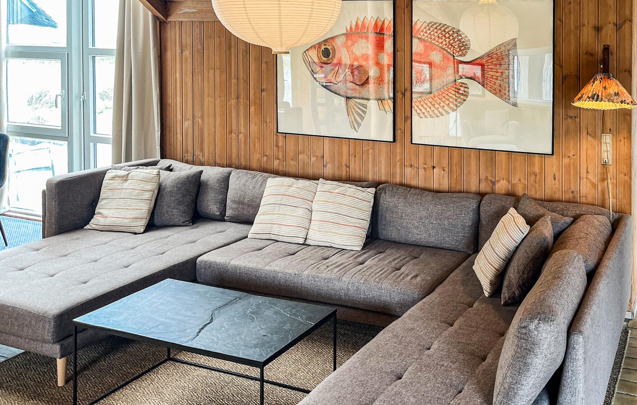 A sectional sofa with striped pillows, a small coffee table, and a fish painting on the wall.