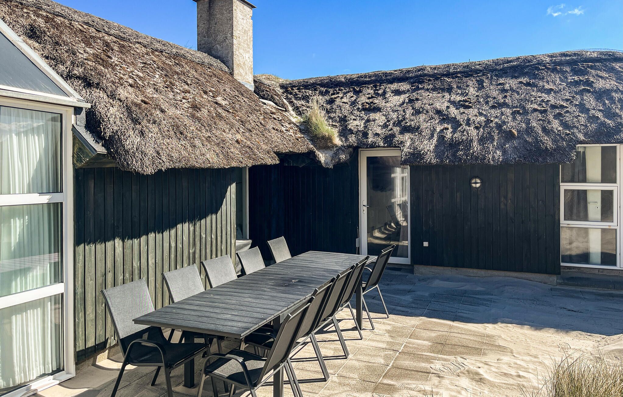 Eine Terrasse mit Tisch und Stühlen, einem Reetdach und einem Holzzaun.