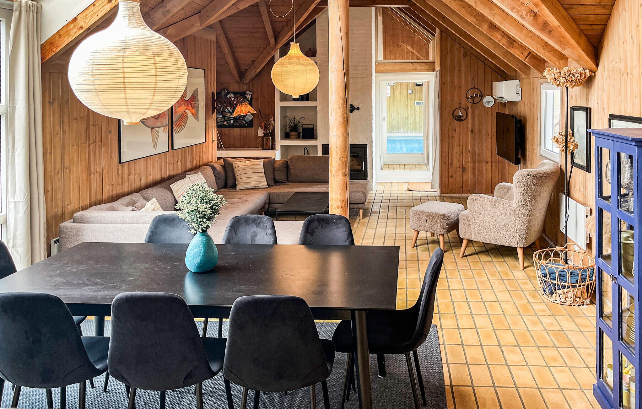En hyggelig indretning med træloft, spiseplads med bord og stole, sofa og pejs.