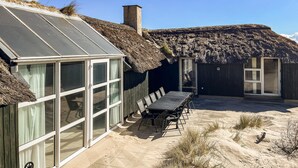 A modern house with a glass conservatory, a thatched-roof structure, and a patio with outdoor seating. - Lovely home in Hvide Sande with sauna (Hvide Sande)