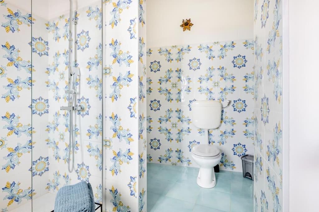 Un baño con azulejos de estampado floral, un inodoro y una zona de ducha.