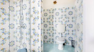 Un baño con azulejos de estampado floral, un inodoro y una zona de ducha.