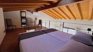 Ein Schlafzimmer mit einem großen Bett, Holzbalken, einem Oberlicht, einem Sessel und Blick ins Freie.
