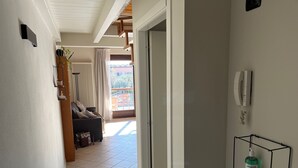Ein Flur, der in einen Wohnbereich mit einer Couch, einem Heizkörper und Blick ins Freie führt.