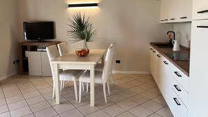 Eine moderne Küche mit weißen Schränken, einem Esstisch mit Stühlen, einem Fernseher und einer Pflanze an der Wand.