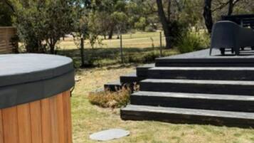 A hot tub with steps leading up to a seating area in a landscaped outdoor setting.