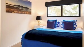Une chambre à coucher avec un lit, une table de chevet, une lampe et une fenêtre donnant sur des arbres.
