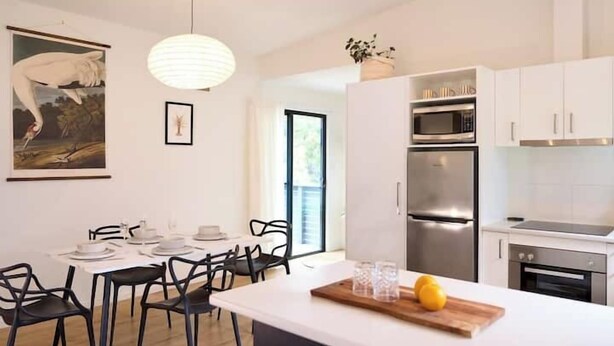 Une cuisine moderne avec des meubles blancs, des appareils en acier inoxydable et un coin repas doté de chaises noires.