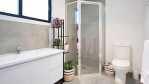 Une salle de bain moderne avec un lavabo, des toilettes et une douche à l’italienne, le tout de couleur blanche.
