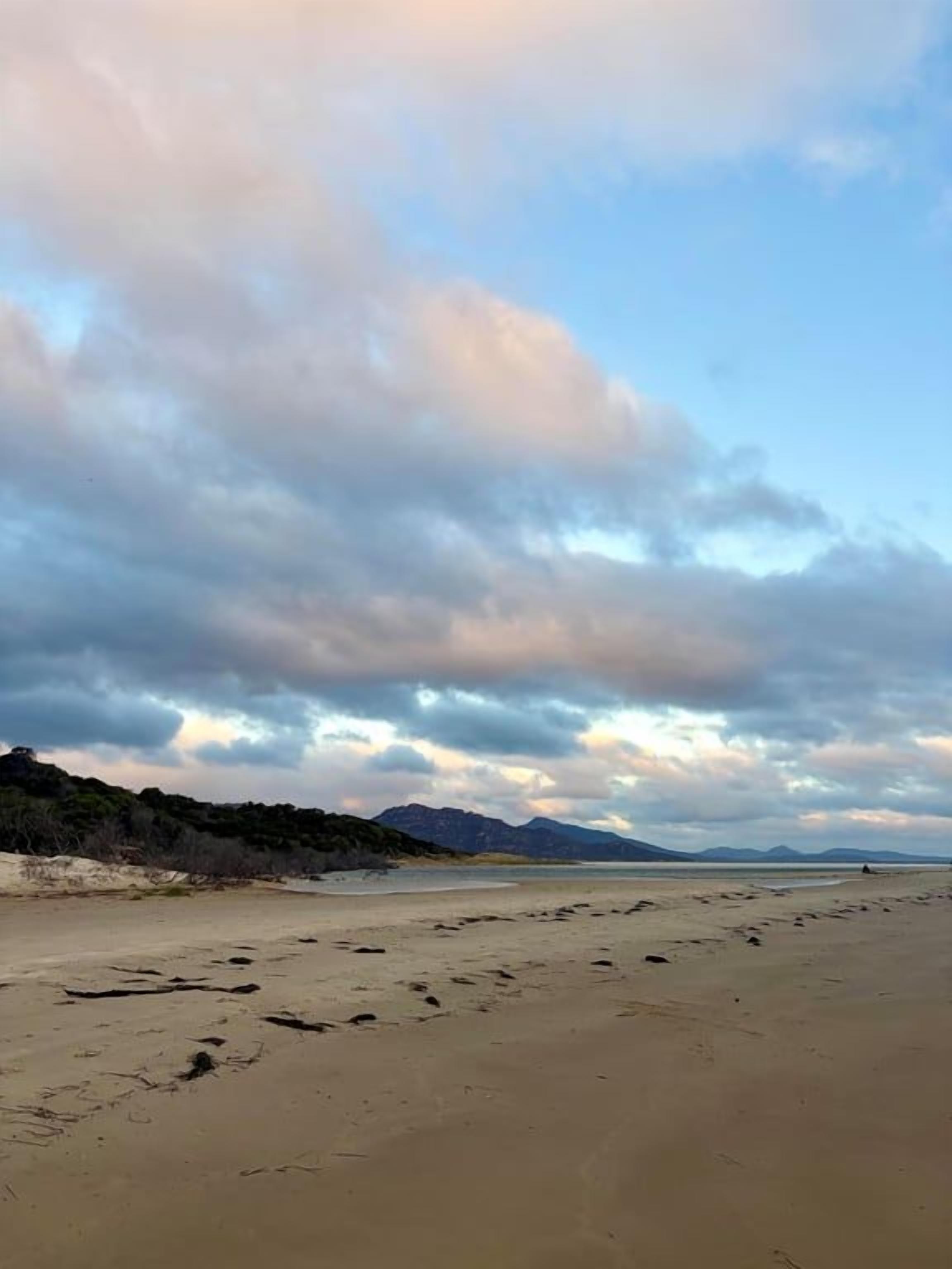 A beach with footprints leading to the water, a clear sky, and distant mountains.