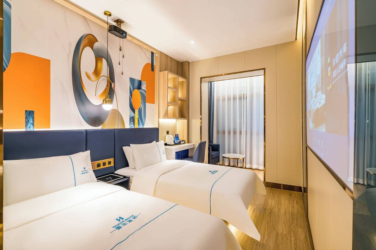 A hotel room with two beds, a desk, a chair, a small table, a TV, and a large window with curtains.