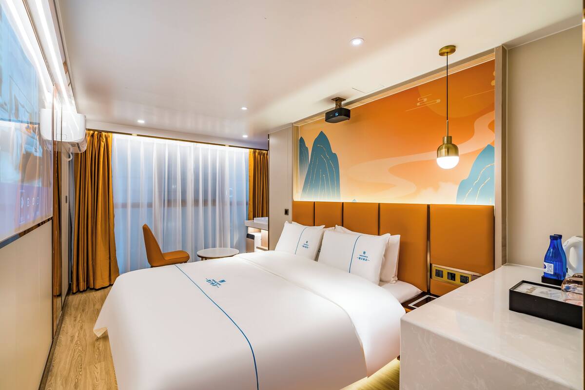 A hotel room with a large bed, a desk, a chair, and a painting on the wall.