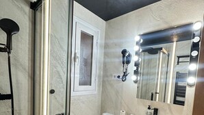 Une salle de bain avec une douche à parois de verre, des toilettes, un lavabo avec un miroir et un meuble-lavabo avec des tiroirs.